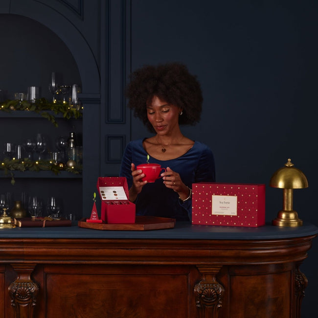 高級バーカウンターの上に、季節限定のティーバッグアソート+茶器のおしゃれな紅茶ギフトセットが置いています。スタイリッシュな女性が赤いティーカップで紅茶を淹れています。